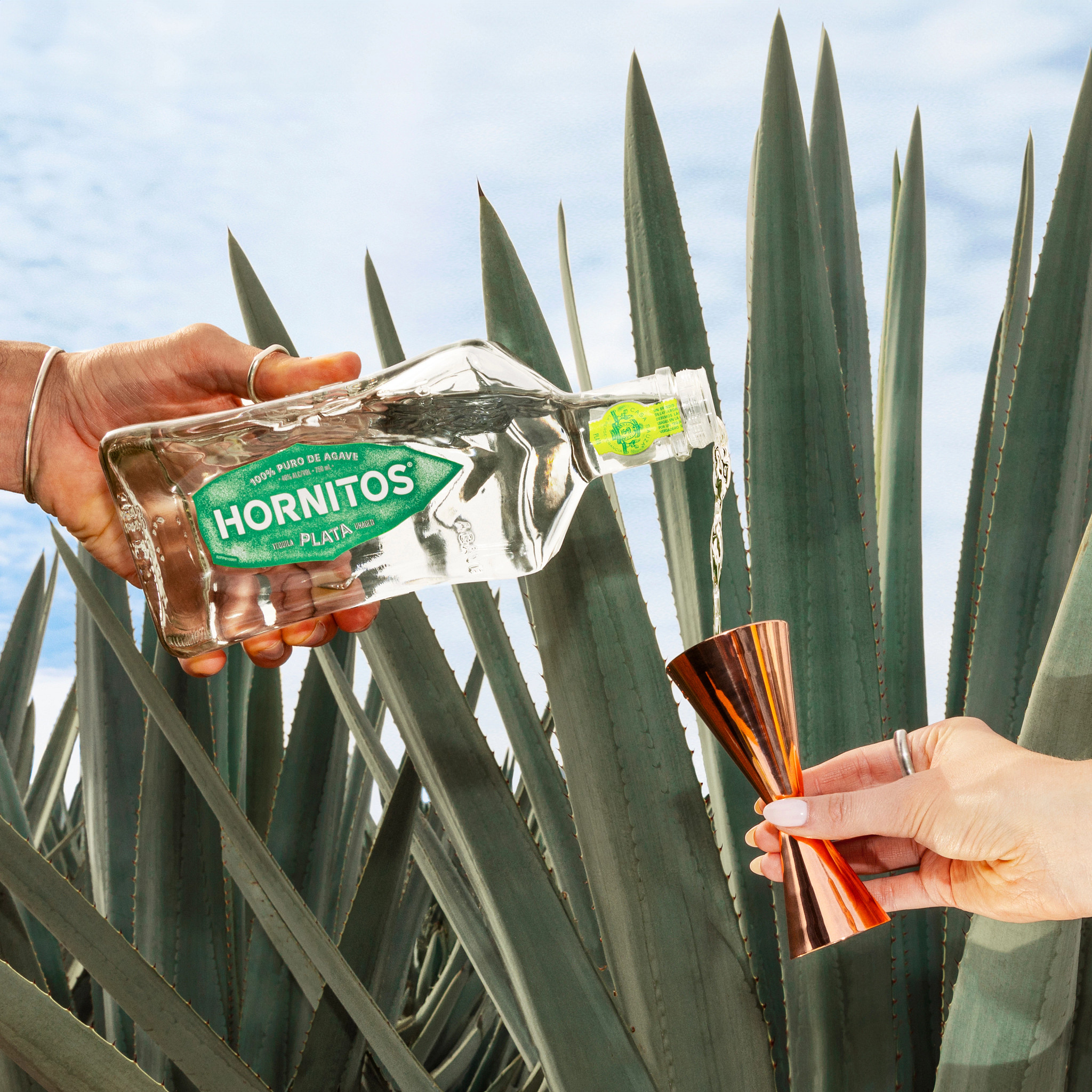 Hands Pouring Tequila Bottle Into Jigger Agave Background Hornitos