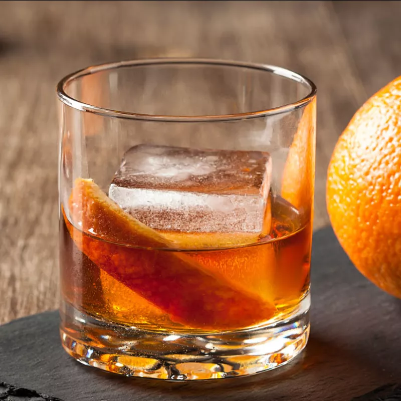 Lifestyle Image of Old Fashioned Cocktail garnished with orange peel and ice 