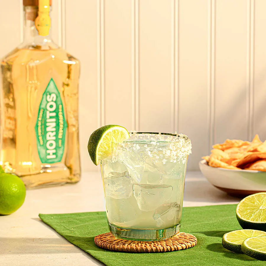 Image of Glass filled with Margarita cocktail and A reposado bottle in background 