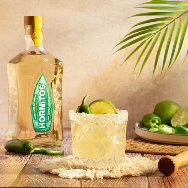 Spicy margarita cocktail with Hornitos Reposado, jalapeño and lime in a salt-rimmed glass on a wooden table.