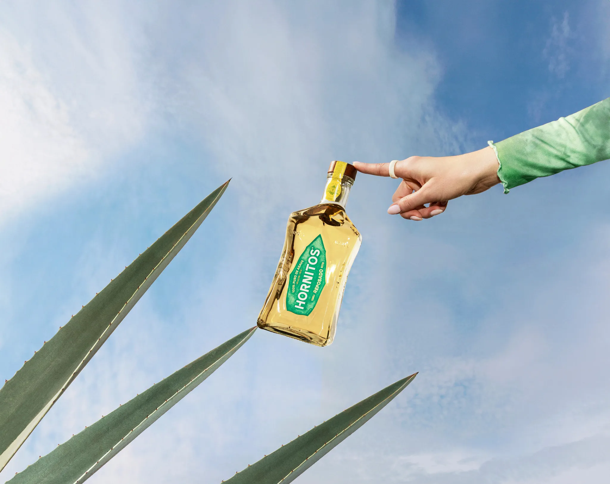 Hand Balancing Tequila Bottle Agave Leaves Sky Background Hornitos